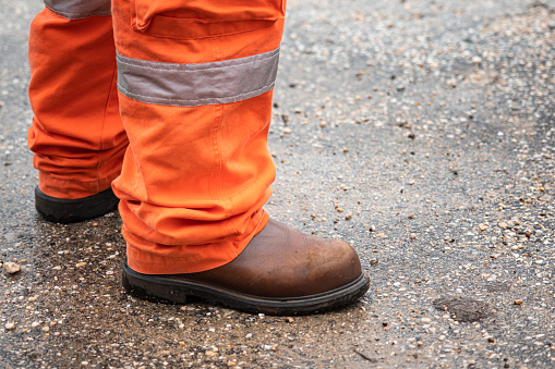 A part of operation staff which is wearied fully PPE such as leather safety shoe and coverall suit. Ready for working in unsafe work place concept action photo. Close-up and selective focus.