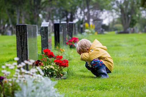 Sad little child, blond boy, standing in the rain on cemetery, sad person, mourning, summer rainy day