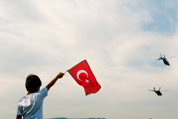 A boy holding a Turkish flag and police helicopters demonstrating in the sky on the liberty day of Izmir. stock photo