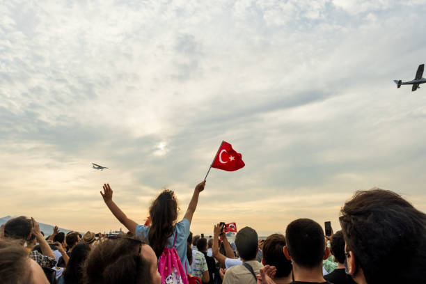 ein flugzeug, das am freiheitstag von izmir für eine demonstration in den himmel fliegt. ein mädchen, das eine türkische flagge im rahmen schwenkt und menschen überfüllt. - april stock-fotos und bilder