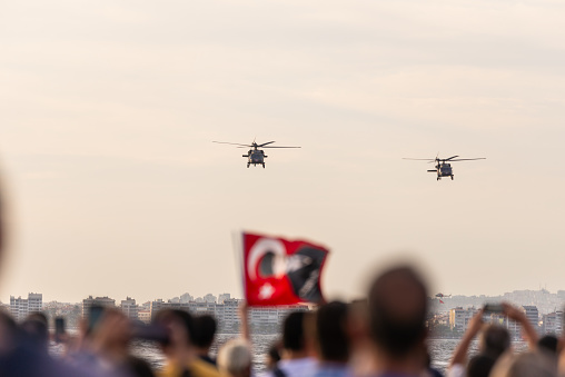 Izmir, Turkey - September 9, 2021: Turkish Police Helicopters demonstrate in the sky celebrations of liberation day of Izmir with a crowd of people holding Turkish flags