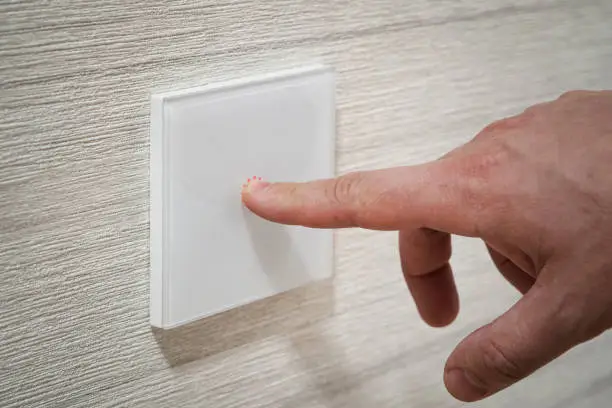 A close-up finger turns on the light on the touch switch. A white modern light switch on a white wall. modern design.