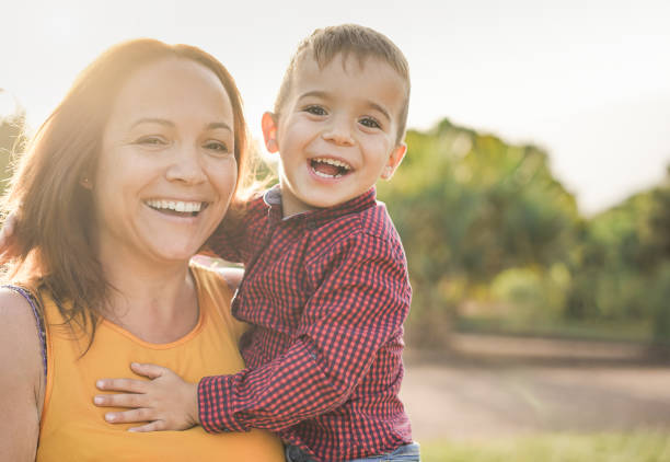 feliz madre latina sosteniendo a su hijo en sus brazos y riendo ante la cámara - madre e hijo aman - niño pequeño fotografías e imágenes de stock