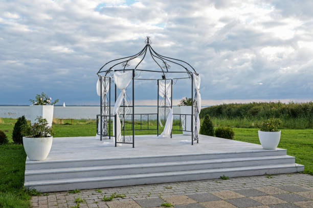 Iron pavilion decorated with white cloths for a wedding ceremony on a platform on the lake shore under a cloudy sky, copy space, selected focus