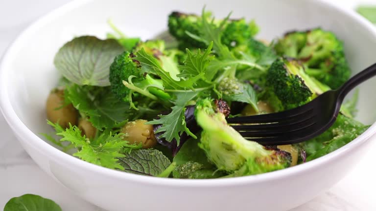 Green salad with grilled broccoli and olives in white bowl.