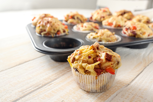 Tasty baked pizza muffins as finger food for a party from yeast dough, tomatoes, vegetables, sausage and cheese on a wooden table, copy space, selected focus, narrow depth of field