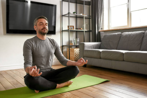 spokojny mężczyzna w słuchawkach medytuje ćwicz jogę w domu - lotus position audio zdjęcia i obrazy z banku zdjęć