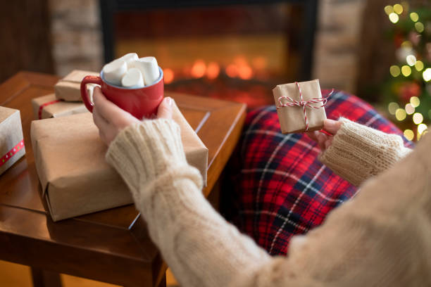 여성은 가족을 위한 선물 상자를 포장한 후 폴라위퍼와 크리스마스 트리 근처에서 격자무늬 앉아 휴식을 코코아와 마시멜로 로 덮었다. - light bulb women inspiration surprise 뉴스 사진 이미지