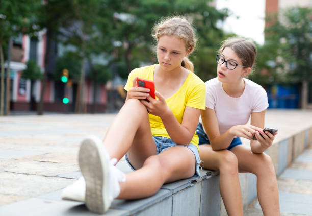 les adolescents partagent des informations entre eux à partir de smartphones tout en se relaxant dans la rue - 12 15 months photos et images de collection