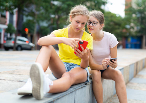 adolescentes compartilham informações uns com os outros a partir de smartphones enquanto relaxam na rua - 12 15 months - fotografias e filmes do acervo