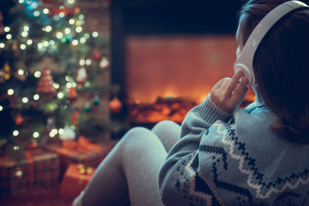 헤드폰을 쓰고 있는 여성은 벽난로 불꽃과 크리스마스 트리 근처에서 겨울 저녁에 앉아 따뜻합니다. - blanket fireplace winter women 뉴스 사진 이미지