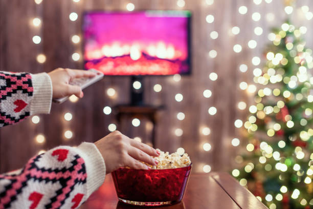 istock Christmas eve. Alone woman eating popcorn, watching tv, switching channels using remote control. Home cinema. Cropped, close up 1341667125