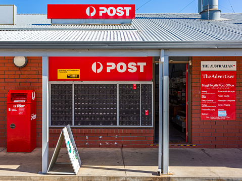 Adelaide, Australia - April 30, 2021:  Magill North 5072 Post Office, St Bernards Rd shopping precinct. Front view showing Australia Post signage, secure private mail boxes, posting box and advertising poster, open front door.  Verandah illuminated by translucent roofing