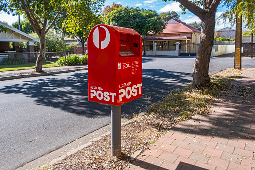 Adelaide, Australia - May 12, 2021: Angus Street, Goodwood: Australia Post Red Street Posting Box surrounded by older established houses in leafy suburban street: T-intersection with classic Stobie power pole