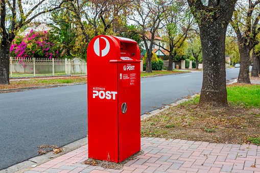 Adelaide, Australia - May 16, 2021: Tusmore Ave, Tusmore; full length view of Australia Post Red Street Posting Box in quiet, leafy established suburban street. Autumn colours, neat front yards, fences,