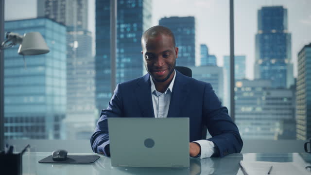 Portrait of Thoughtful Black Businessman Working on Laptop Computer in His Big City Office. Charismatic Digital Entrepreneur does Data Analysis for e-Commerce Strategy assessment. Zoom In Front View