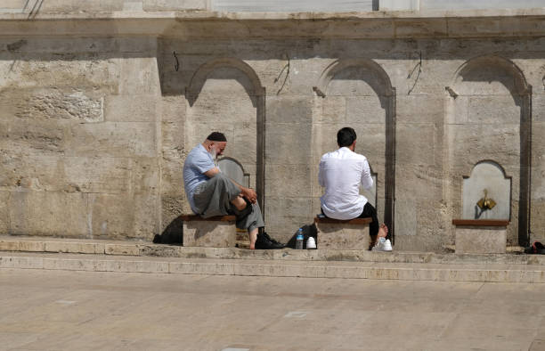 Muslim mans taking ritual ablution in wudhu station at mosque in ISTANBUL - September, 2021. Faucets for washing hands and feet before the prayer and stones to sit on near mosque in Islamic culture. Muslim mans taking ritual ablution in wudhu station at mosque in ISTANBUL - September, 2021. Faucets for washing hands and feet before the prayer and stones to sit on near mosque in Islamic culture. turkey koran people design stock pictures, royalty-free photos & images