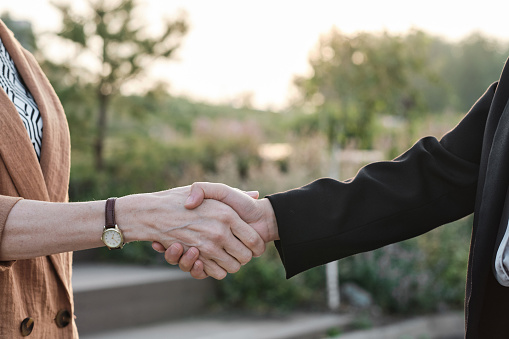 Horizontal medium close-up shot of unrecognizable businesswomen greeting each other with handshake in urban park in evening