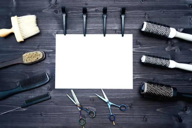 Hairdresser tools on wooden background. Blank card with barber tools flat lay. Top view on wooden table with scissors, comb, hairbrushes and hairclips with empty white paper, free space. Barbershop, manhood concept