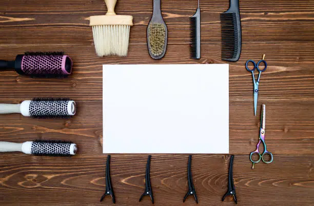 Hairdresser tools on wooden background. Blank card with barber tools flat lay. Top view on wooden table with scissors, comb, hairbrushes and hairclips with empty white paper, free space