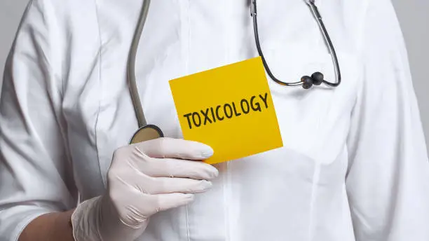 Photo of Cropped view of doctor in a white coat and sterile gloves holding a note with text - Toxicology