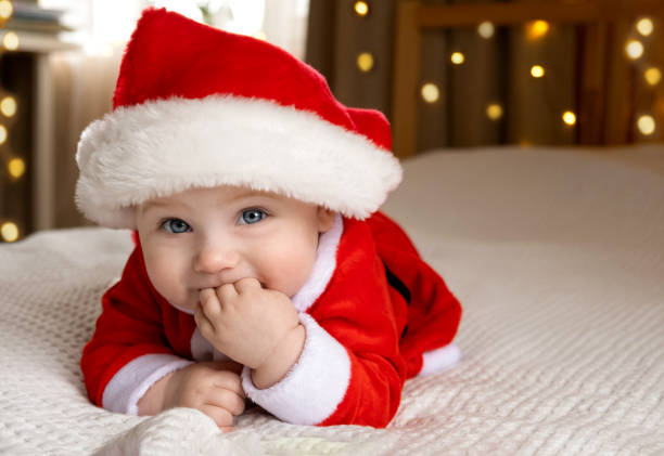 улыбающийся ребенок в красной шляпе санта-клауса празднует рождество. милый новорожденный ребенок в рождественской шапке, лежащей на вяза� - santa hat фотографии стоковые фото и изображения
