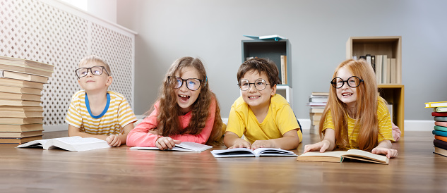 Four cute children in glasses lying on the floor indoors with books. Concept of hobby and education.