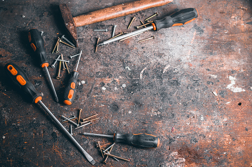 Screwdrivers, screws and hammer on a wooden workbench. Top view on working tools with space for text. Construction tools on work wooden table. Background of various construction tools.