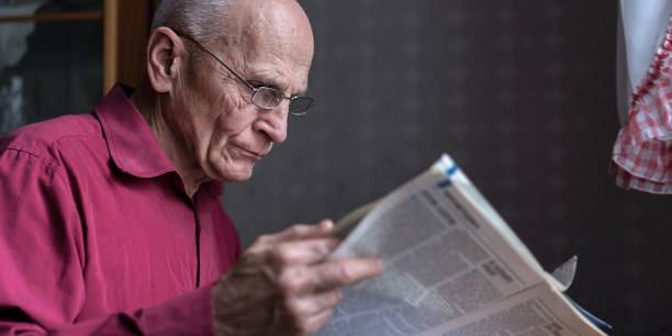 istock Older man wearing eyeglasses reading newspaper side view 1341696756
