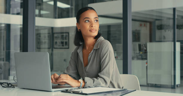 photo d’une belle jeune femme perdue dans ses pensées alors qu’elle utilisait son ordinateur portable dans un bureau moderne - thinking women businesswoman business photos et images de collection