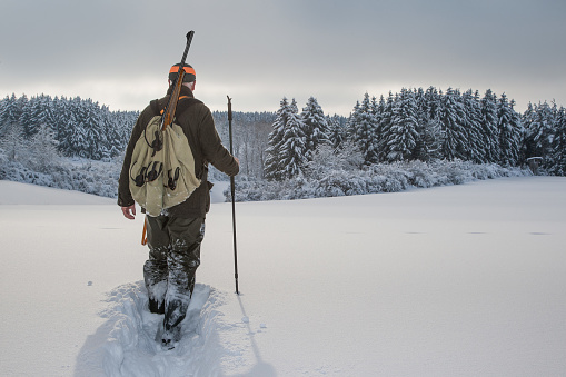 In a picturesque winter landscape a hunter walks down through the fresh, deep snow into the small valley.\