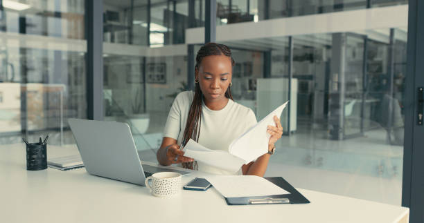 shot of a beautiful young woman doing some paperwork in a modern office - paper document notebook laptop imagens e fotografias de stock
