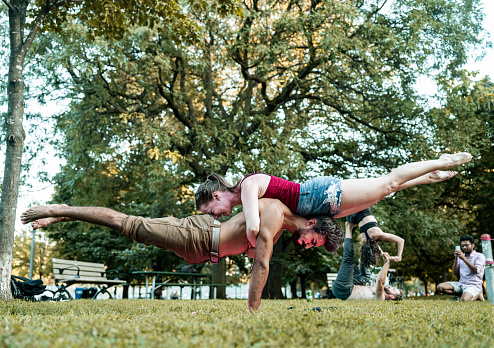 Group of young People practising Acro Yoga. All dressed in casual sport clothing. Various backgrounds and nationalities. Exterior of public park in sunset.