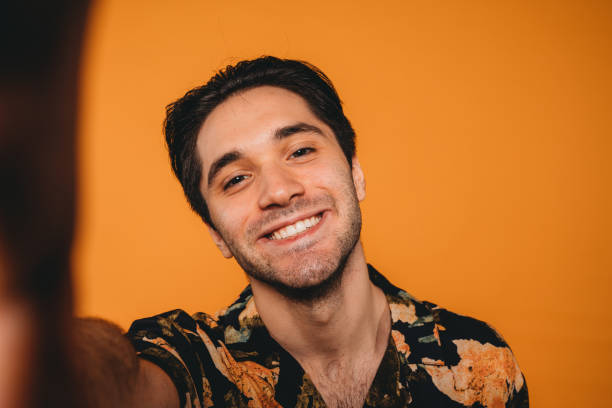 vista pov de un hombre adulto joven tomándose una selfie sobre un fondo naranja - copy space one person vertical 1970s style fotografías e imágenes de stock