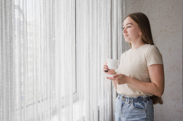 istock Young Woman Standing at Window with Coffee 1341701254