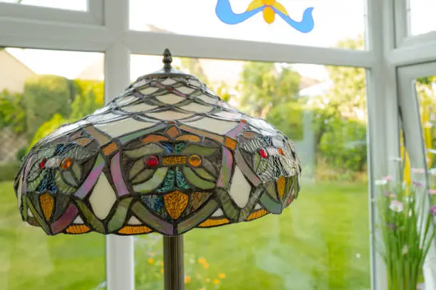 Shallow focus of an ornate, coloured-glass floor lamp seen in a garden conservatory.  A lush lawn can be seen in the background.