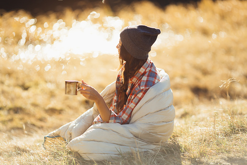 Beautiful traveler woman hiking in the mountains with a cup of drink near lake, camping travel concept. Girl on vacation enjoying the beauty of nature.