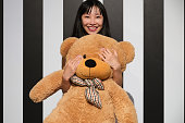 Young asian woman hugging a teddy bear standing on a striped room floor.