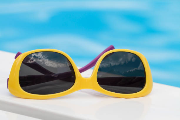 istock Children sunglasses lying on a deck-chair on blue water background 1341711317