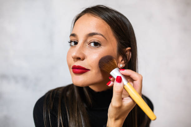 eine schöne junge frau, die mit einem großen pinsel ein rouge anwendet - roter lippenstift stock-fotos und bilder