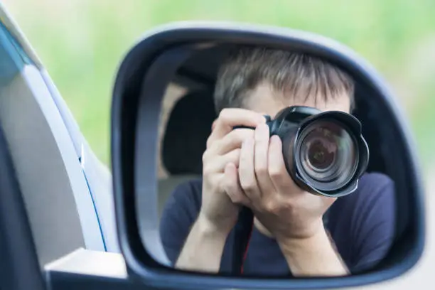Photo of A man is taking photo someone or something from an open car window. Reflection in the side mirror of the car