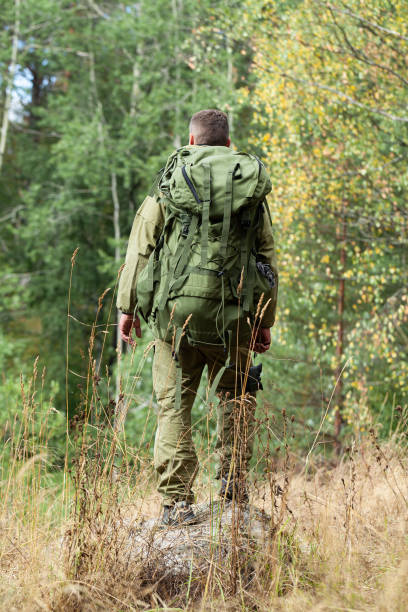 istock Young man travelling alone with a backpack. Concept of active tourism, camping in the forecast, trekking and hiking during vacations. Green background. Copy space for text 1341712564