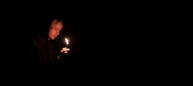 calm mysterious story teller teenager with candle in hand, Halloween advertising concept of panoramic picture with black background space for text or copy