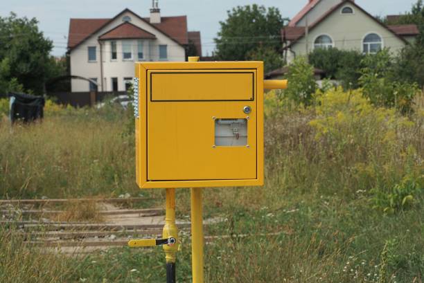 one yellow metal square gas meter on an iron pole on the street against a background of green vegetation