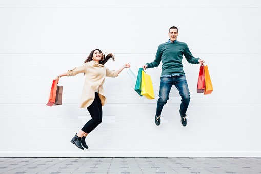Closeup of woman and man jumping with shopping bags