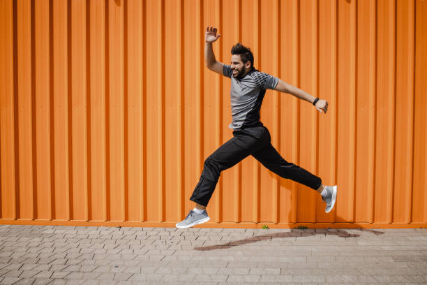 a young man in sportswear jumping in front of the orange wall