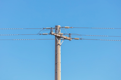 Photograph of a concrete telephone post and cables against a blue sky
