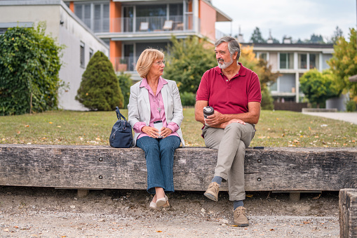 Shot of a senior Caucasian couple enjoying coffee while sitting on a bench in a public park. Smiling enjoying life.