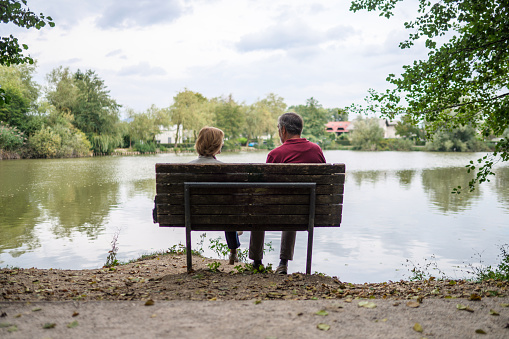 Senior couple sitting on a bench next to a lake in a public park. Enjoying the view over the lake.