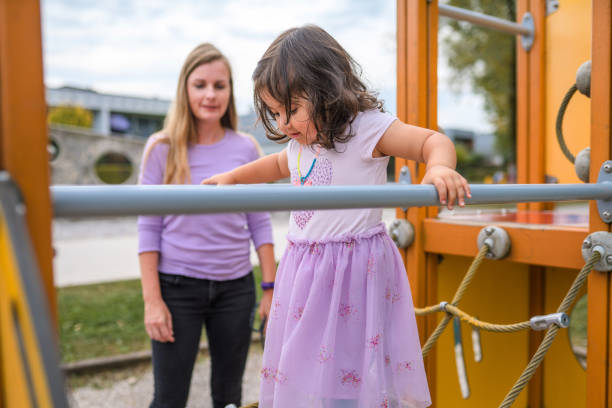 Shot of a young girl playing in public a playground in the park while her mother is watching.
